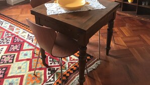 Ein Essbereich mit Holztisch, Stühlen, einem gemusterten Teppich, einem Schrank mit Glastüren, einer geschlossenen Holztür und einem Fernseher auf einem Holzschrank.