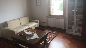 Ein Wohnzimmer mit einer Couch, einem Couchtisch aus Holz mit einer Ablage, einem gemusterten Teppich und einem Schrank mit Glastüren.