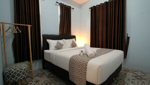 A neatly arranged hotel room with a bed, a bedside table, a hanging coat rack, and patterned floor tiles.
