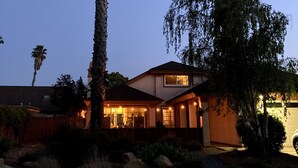A residential house with a tall palm tree, a driveway, and a well-lit front porch. - Private SLO Retreat - Bishop Peak Views, Near Cal Poly, Downtown & Wineries (San Luis Obispo)