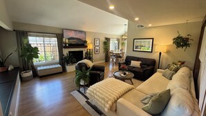 A spacious living room with a fireplace, a sofa, a coffee table, and a dining area in the background. - Private SLO Retreat - Bishop Peak Views, Near Cal Poly, Downtown & Wineries (San Luis Obispo)