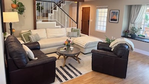 A living room with a sofa, two armchairs, a coffee table, a lamp, a potted plant, and a staircase leading to another level. - Private SLO Retreat - Bishop Peak Views, Near Cal Poly, Downtown & Wineries (San Luis Obispo)
