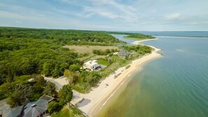 Vista aérea de una propiedad costera con playa arenosa, una gran masa de agua y abundante vegetación.