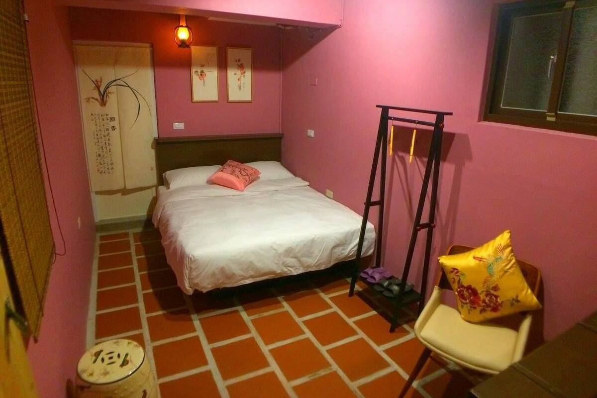 A small bedroom with a bed, a chair, a ladder, and a window.
