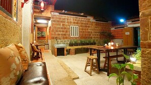 An outdoor patio area with a brick wall, a wooden table, a bench, and potted plants. - Zhu Shan Homestay (Jincheng)