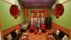 A room with green walls, orange tiled floor, two black sofas with red cushions, a small table with a plate of food, and traditional red lanterns. - Zhu Shan Homestay (Jincheng)