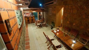 A dining area with a long wooden table and chairs, a bar area with stools, and a stone wall with a tiled pattern. - Zhu Shan Homestay (Jincheng)