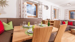 Un coin repas avec une table en bois dressée pour quatre personnes, entourée de canapés marron ornés de coussins rouges et verts.