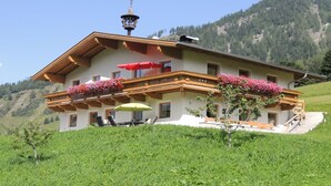 Un chalet à deux étages doté d’un balcon, d’un espace salon extérieur et de jardinières.