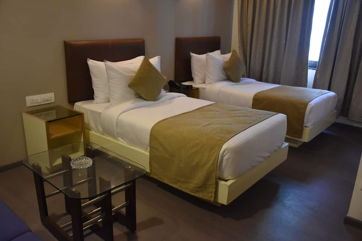 Quarto de hotel com duas camas, uma mesa de vidro e uma mesinha de cabeceira.