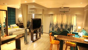 A hotel room with a bed, a TV, a dining area with chairs, and a sofa.
