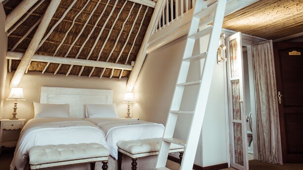 A bedroom with two beds, a ladder, and a wooden ceiling.
