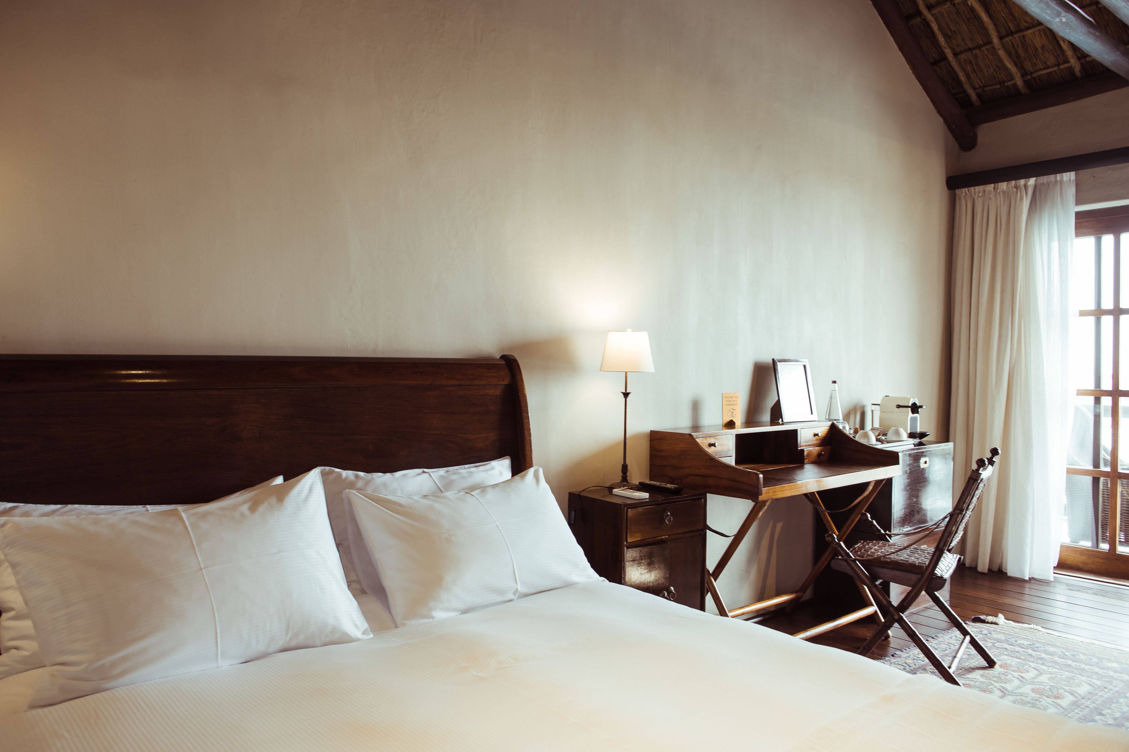 A hotel room with a large bed, a desk with a lamp, and a chair.