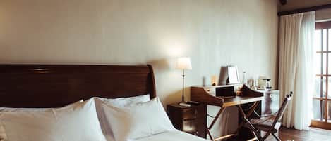 A hotel room with a large bed, a desk with a lamp, and a chair.