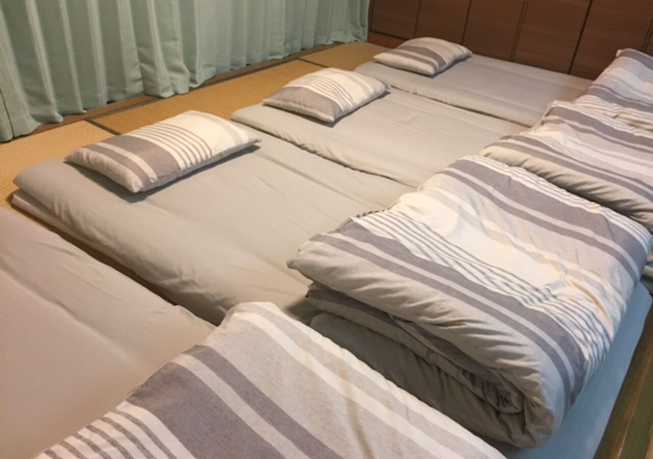 A room with multiple beds arranged in a row, each with striped bedding and pillows.