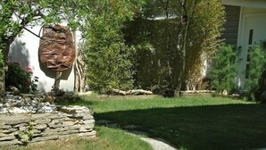 A landscaped garden with a stone wall, a variety of shrubs, and a large tree. - nicely furnished and comfortable, close to the beach (Hourtin-Plage)