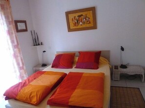 A bedroom with a bed, pillows, a nightstand, a lamp, and a painting on the wall.