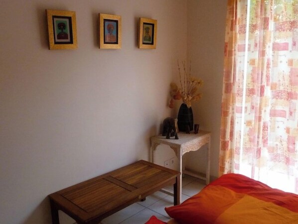A bedroom with a bed, a wooden bench, a small table with a vase, and three framed pictures on the wall. - Very nice, comfortable house, ideal location G0125 (Hourtin-Plage)