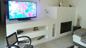 A living room with a flat-screen TV on a white entertainment unit, a black chair, and a white sofa. - nicely furnished and comfortable, close to the beach (Hourtin-Plage)
