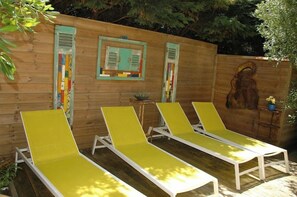 Three sun loungers with white frames and yellow cushions, positioned in front of a wooden wall with a window and a door.