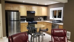 A modern kitchen with stainless steel appliances, wooden cabinets, and a glass dining table with leather chairs. - Executive Suite with commanding views - Claudette Ct. (Victoria)