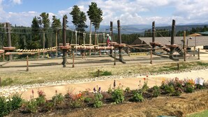 An outdoor adventure course with wooden structures and ropes, surrounded by a landscaped garden with various flowers and a clear view of mountains in the background. - Spring Break, Ski-in/out, 5-star, 2BR, sleeps 8 (Breckenridge)