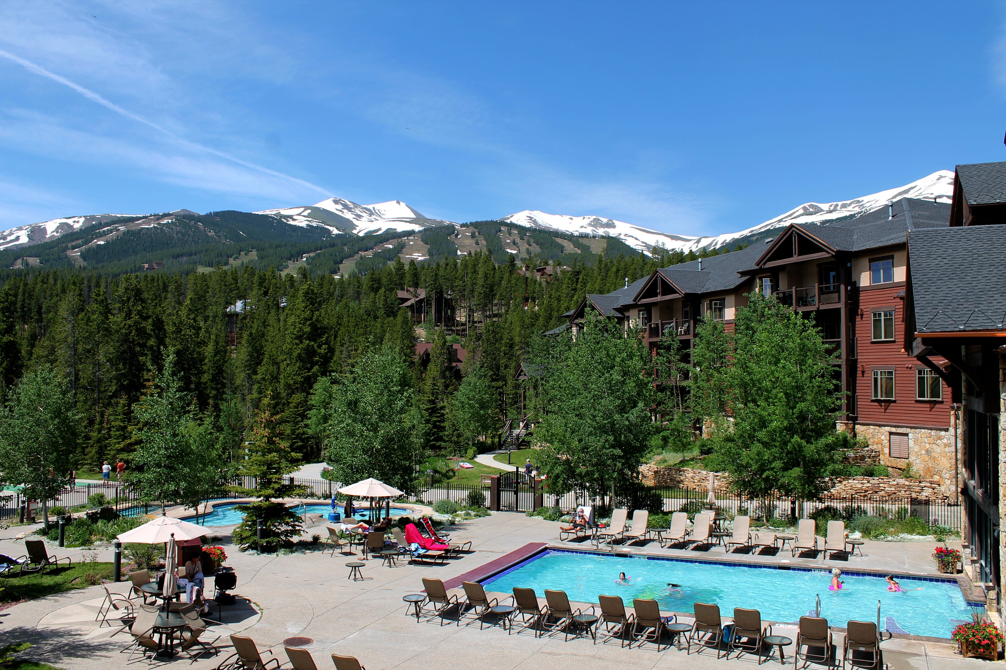 Ein Resort mit Poolbereich, Liegestühlen und Blick auf schneebedeckte Berge.