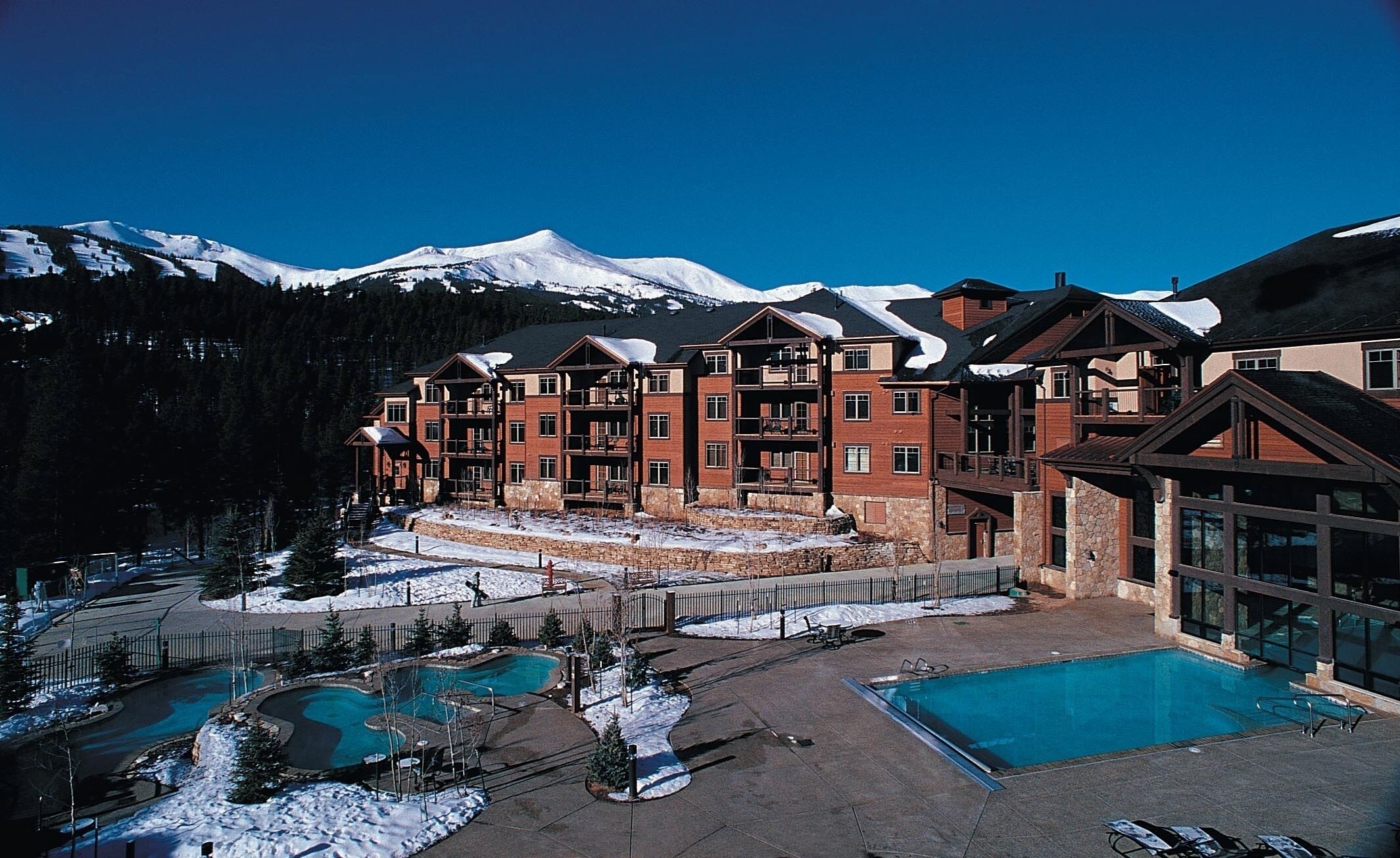Um hotel com vários andares e área de piscina, rodeado por montanhas cobertas de neve.