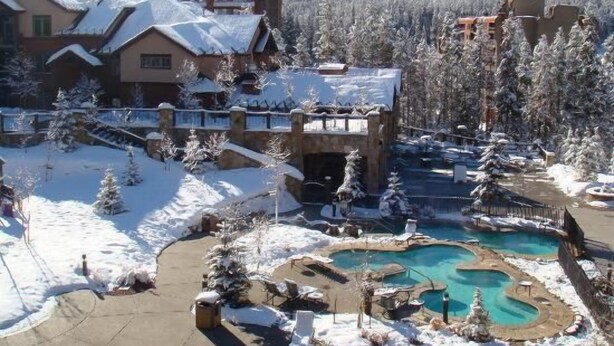 A resort with a pool area surrounded by snow-covered trees and a mountain in the background. - Spring Break, Ski-in/out, 5-star, 2BR, sleeps 8 (Breckenridge)