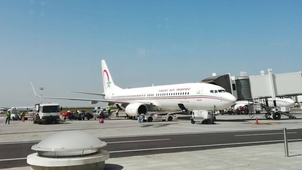 A large airplane parked at an airport gate with ground support equipment and personnel.