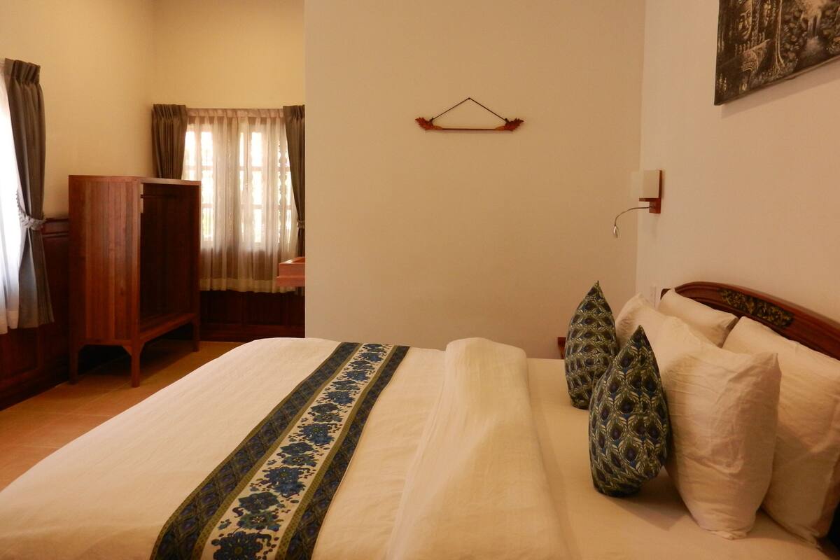Una cama bien tendida con una colcha decorativa, un armario de madera y una lámpara de pared.