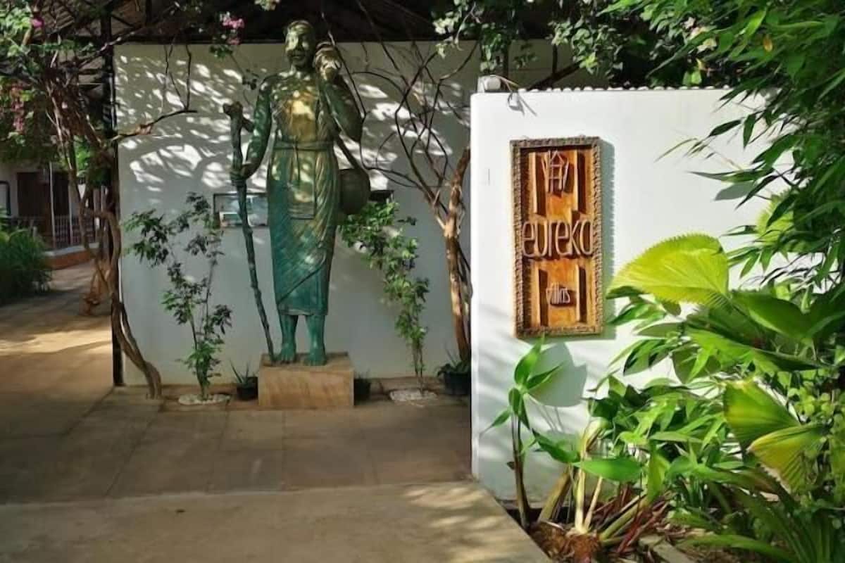 Una estatua en un jardín con un muro blanco y un letrero de madera.