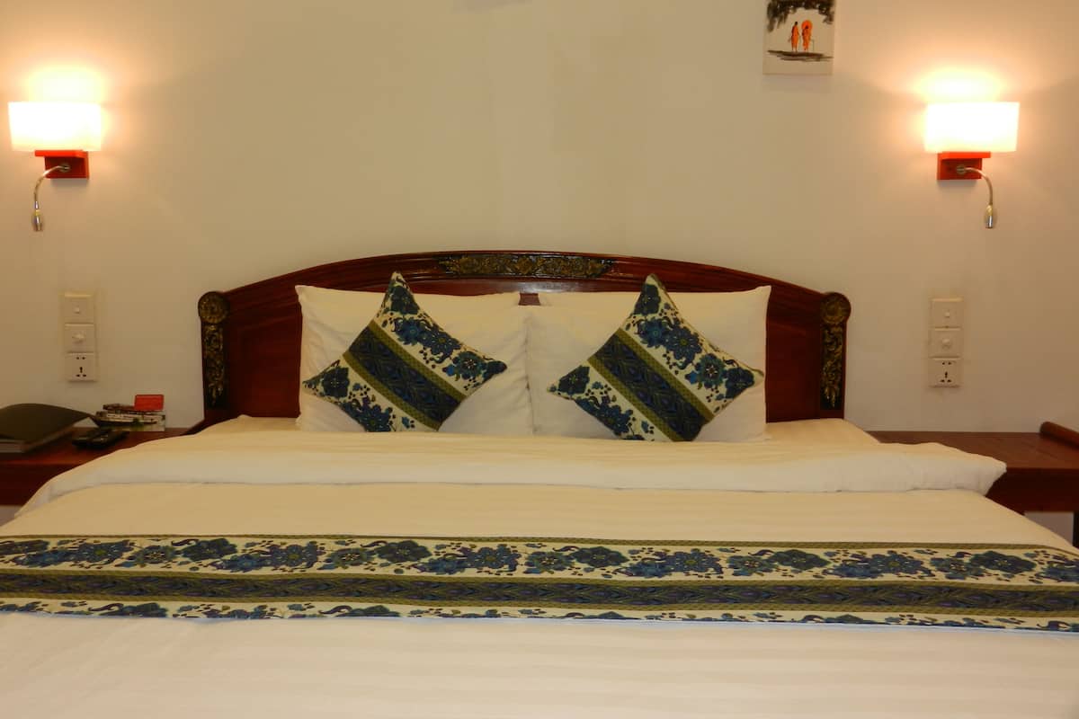 Una cama bien hecha con una colcha de estampado floral y dos almohadones decorativos. Hay dos lámparas de pared a cada lado de la cama.