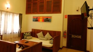 A room with a wooden sofa, a small table, a television mounted on the wall, and a painting of a sunset. - Eureka Villas Siem Reap (Siem Reap)