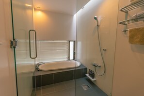 A modern bathroom with a glass-enclosed shower, a freestanding bathtub, and a window with blinds. - The:MOVES-Musée Villa- (Nakijin)