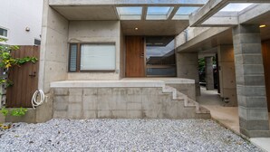 A modern building with a concrete exterior, a wooden door, and a gravel driveway. - The:MOVES-Musée Villa- (Nakijin)