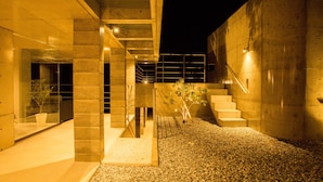 A modern building with a concrete exterior, a staircase, and a small garden area with gravel and plants. - The:MOVES-Musée Villa- (Nakijin)