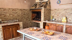 Een keuken met een betegelde achterwand, houten kastjes, een betegelde tafel en een inbouwoven.