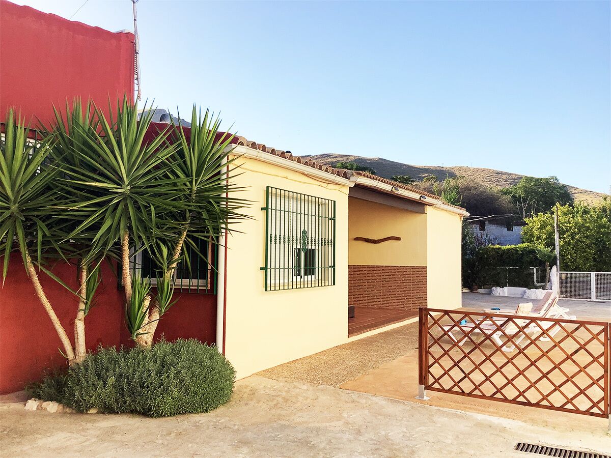A small building with a yellow exterior, a red wall, and a gated entrance.