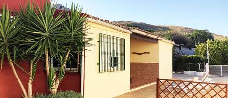 A small building with a yellow exterior, a red wall, and a gated entrance.