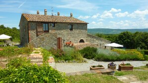 Un edificio in pietra con tetto in tegole, una piccola finestra e un'entrata. Davanti all'edificio si apre un giardino con diverse piante e fiori.