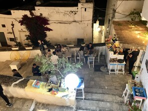 Un patio con mesas al aire libre, un puesto de mercado pequeño y una escalera que sube a un nivel superior.