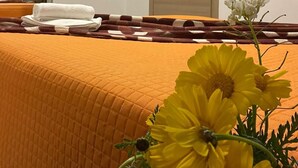 Una camera d'albergo con un letto ricoperto da una coperta arancione, una porta in legno, un condizionatore d'aria e uno scaffale con articoli da toilette.