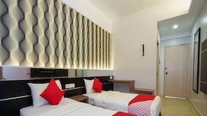 A hotel room with two beds, each with white bedding and red accents, a modern wall panel, and a door to the right. - Hotel O Hotel Orchard Inn (Lumut)