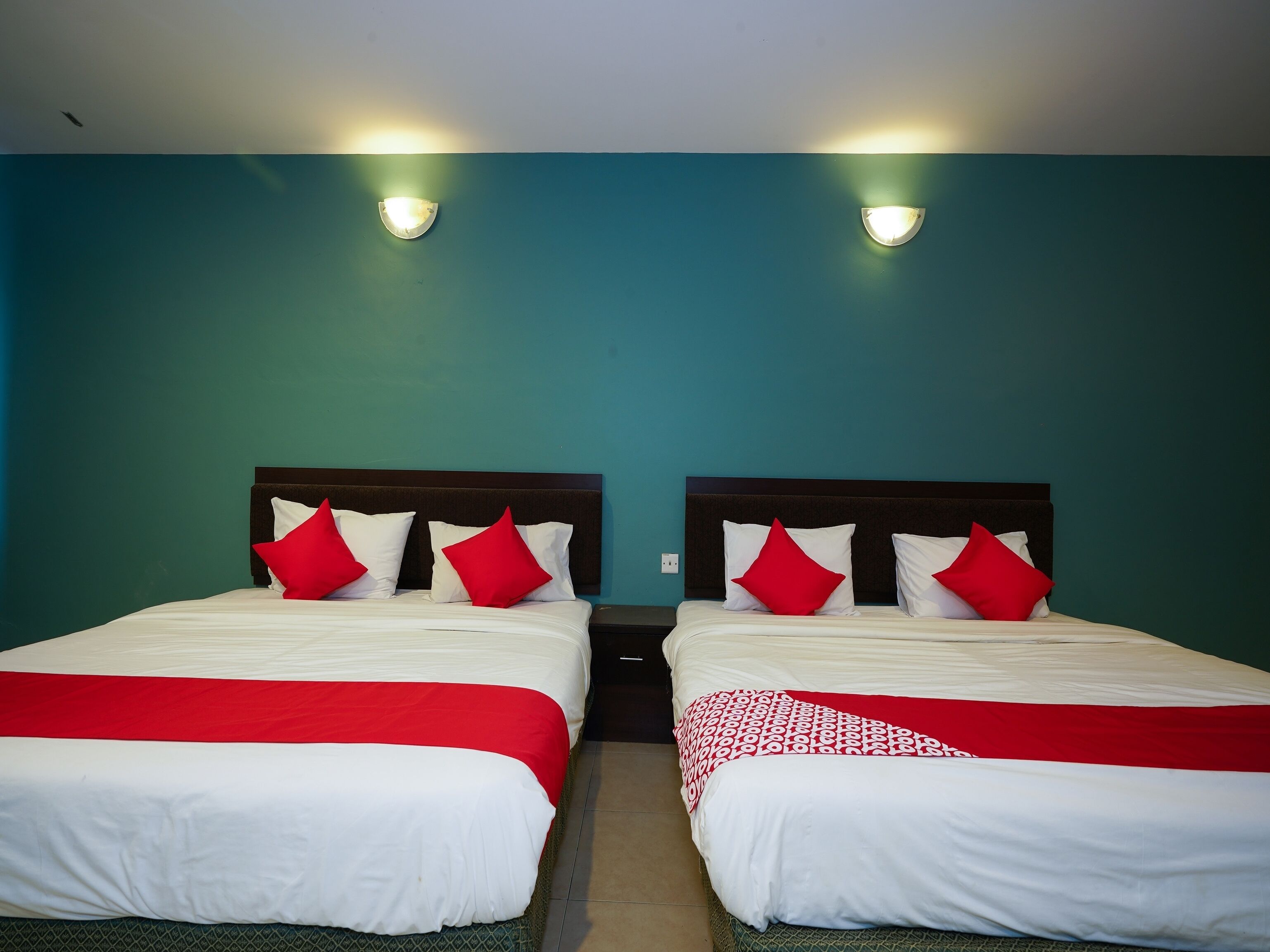 A twin room with two beds, each with white bedding and red accents, against teal walls.