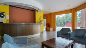 A reception area with a curved counter, two blue armchairs, a wooden coffee table, and a large window offering a view of the outdoors. - Hotel O Hotel Orchard Inn (Lumut)