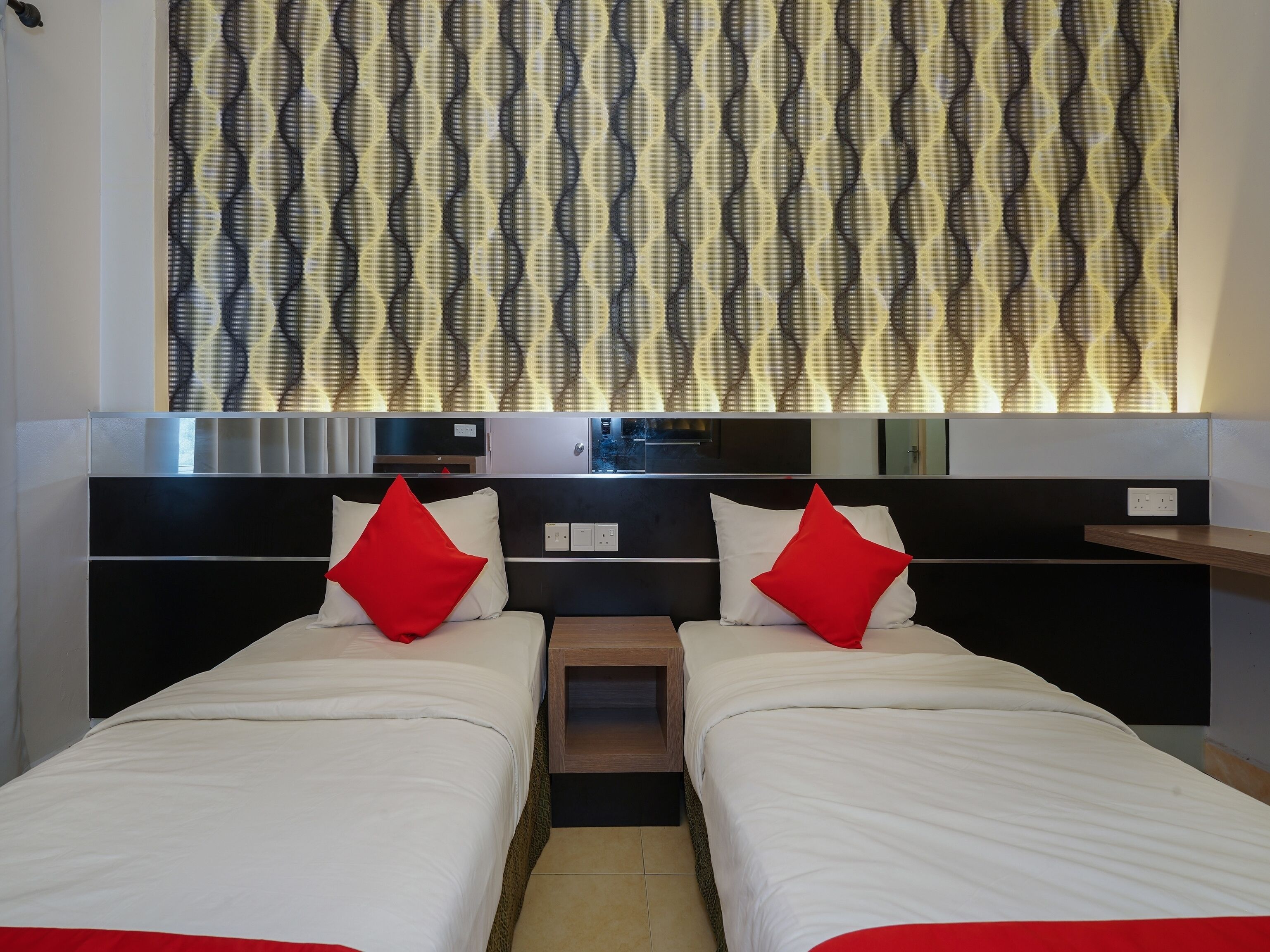 A hotel room with two beds, a modern headboard with a wavy pattern, and a small wooden nightstand.
