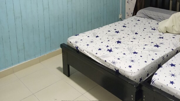Une pièce avec un lit, un petit tabouret, un mur orné de lignes verticales et un rideau.