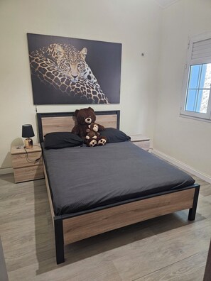 En seng med mørkegrå madras, et træhovedgærde og en bamse og en abe som nussedyr.