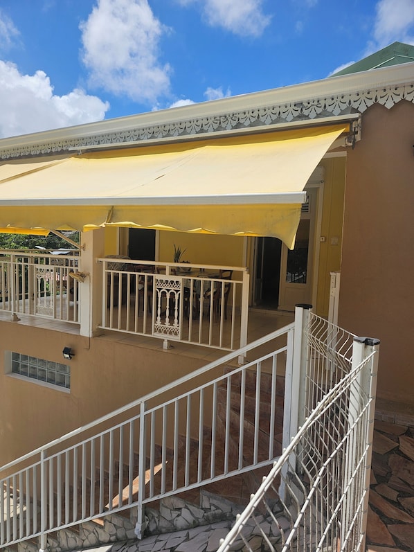 A building with a balcony, a covered area with a railing, and a staircase with a metal railing.